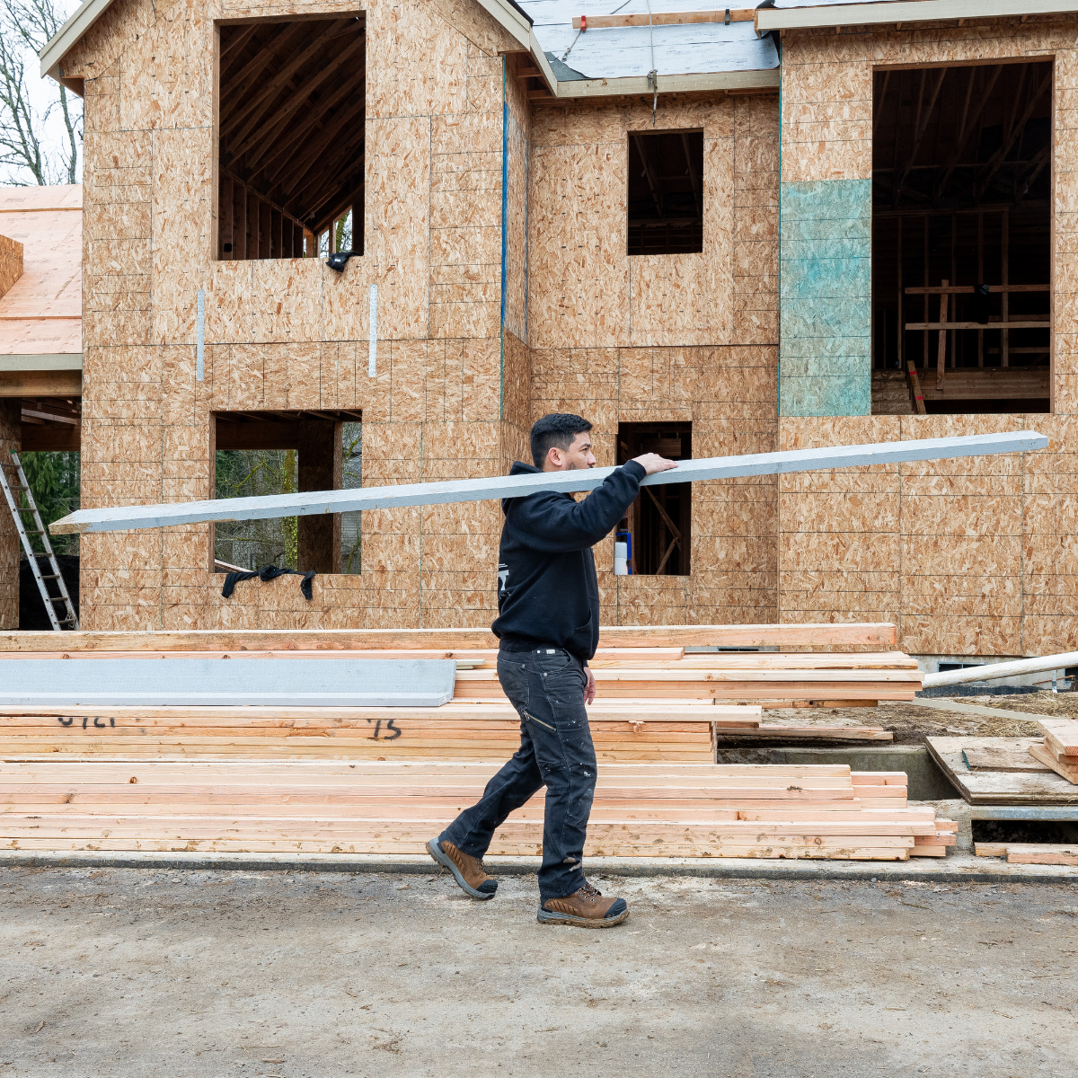 Man with Chinook Footwear work boots on construction site in front of new build home carrying lumber