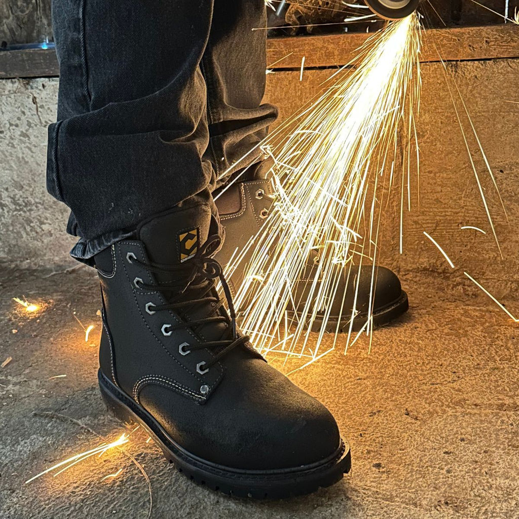 A worker wearing sturdy black work boots stands on a concrete floor, surrounded by bright sparks from a metal grinder. The boots showcase reinforced stitching, a rugged build, and reliable protection, ideal for tough industrial tasks and hazardous environments.