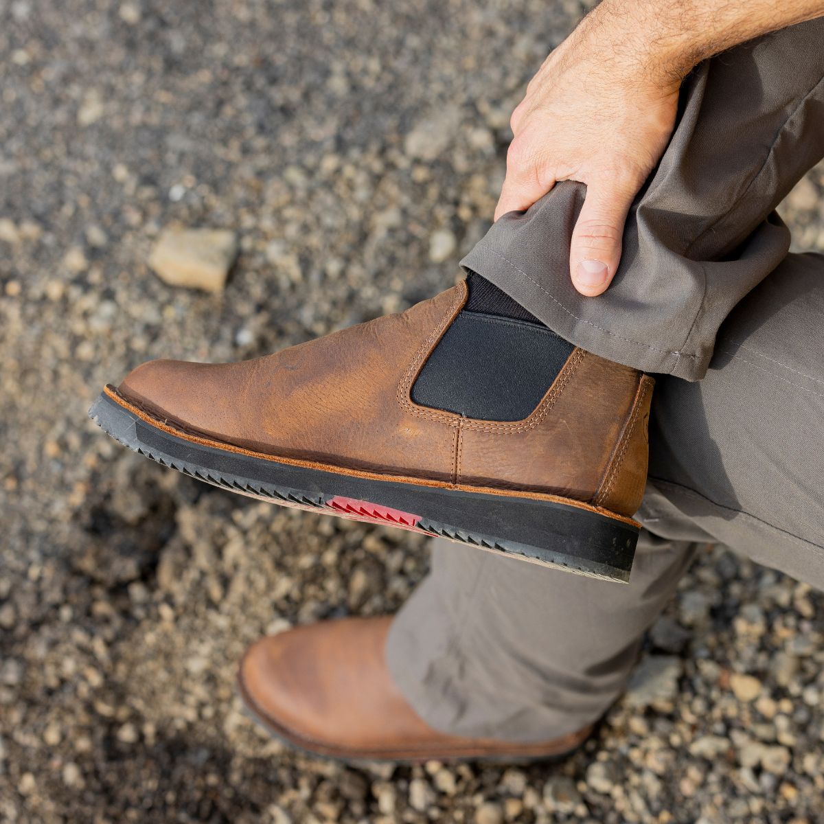 A man adjusting his Romeo Heritage boots in Brown. These stylish slip-on boots feature elastic side panels and a rugged sole, combining durability and comfort for versatile, all-day wear.
