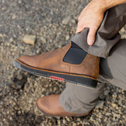 A man adjusting his Romeo Heritage boots in Brown. These stylish slip-on boots feature elastic side panels and a rugged sole, combining durability and comfort for versatile, all-day wear.